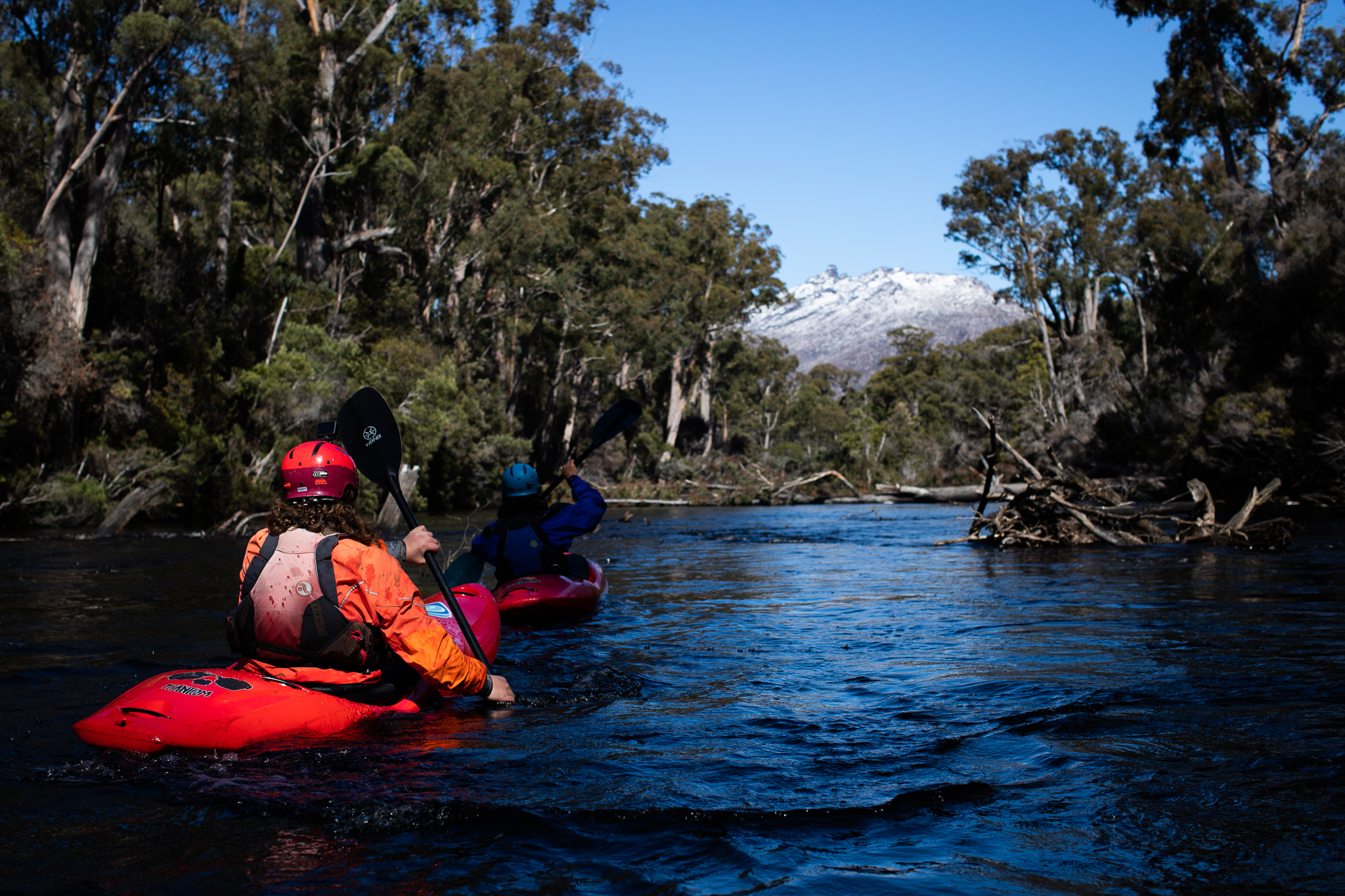 two kayakers paddling away from the camera towards a snowy mountain